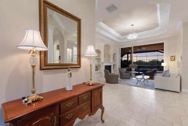 interior space with visible vents, crown molding, a tray ceiling, ceiling fan with notable chandelier, and a fireplace