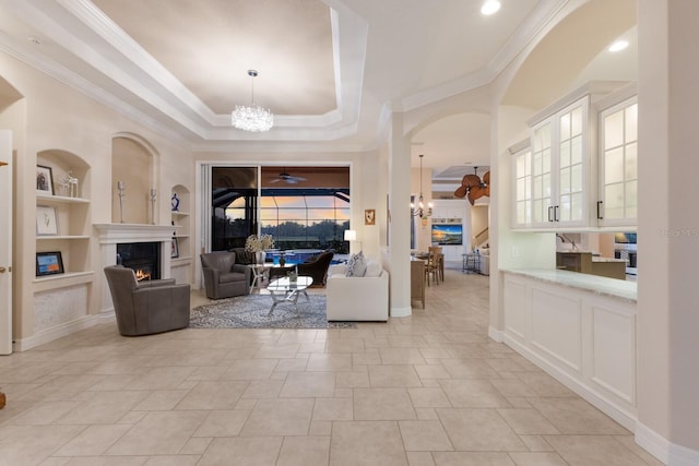 living area featuring built in shelves, baseboards, a fireplace, crown molding, and a raised ceiling