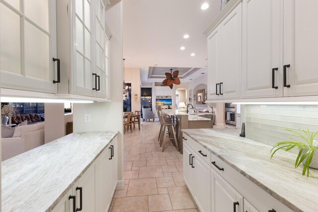 kitchen with open floor plan, light stone counters, recessed lighting, arched walkways, and white cabinetry