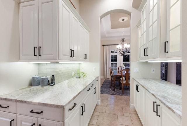 kitchen with light stone countertops, a tray ceiling, decorative backsplash, white cabinetry, and a chandelier