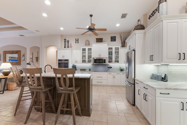 kitchen with visible vents, ceiling fan, appliances with stainless steel finishes, white cabinetry, and a kitchen bar