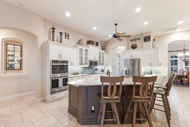 kitchen featuring a kitchen bar, a center island with sink, appliances with stainless steel finishes, white cabinets, and decorative backsplash