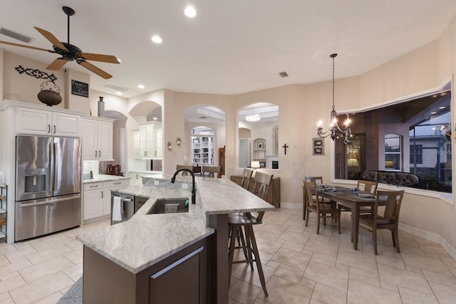 kitchen featuring light stone countertops, visible vents, a sink, appliances with stainless steel finishes, and ceiling fan with notable chandelier