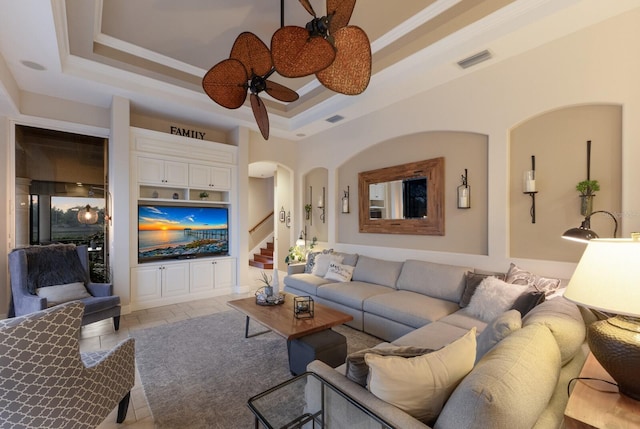 living room with visible vents, a ceiling fan, a tray ceiling, arched walkways, and stairs