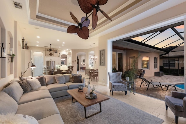 living room with visible vents, ceiling fan with notable chandelier, a tray ceiling, arched walkways, and crown molding