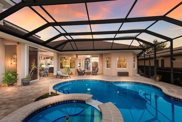 pool at dusk featuring a lanai, a pool with connected hot tub, and a patio