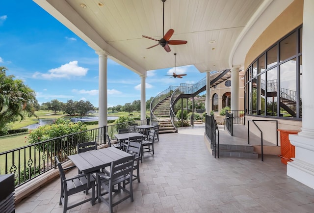 view of patio featuring outdoor dining area, stairs, a ceiling fan, and a water view