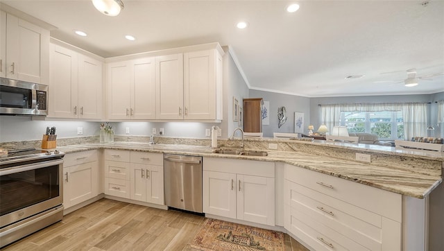 kitchen featuring a peninsula, a sink, stainless steel appliances, white cabinets, and crown molding