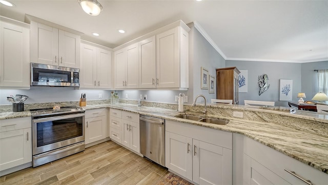 kitchen with light wood finished floors, crown molding, stainless steel appliances, white cabinetry, and a sink