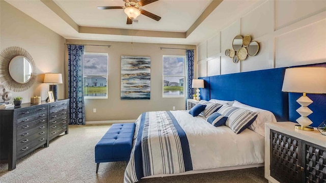 carpeted bedroom with a raised ceiling, a ceiling fan, and baseboards