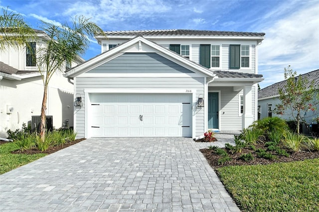 traditional-style house featuring a tiled roof, decorative driveway, central AC unit, and an attached garage