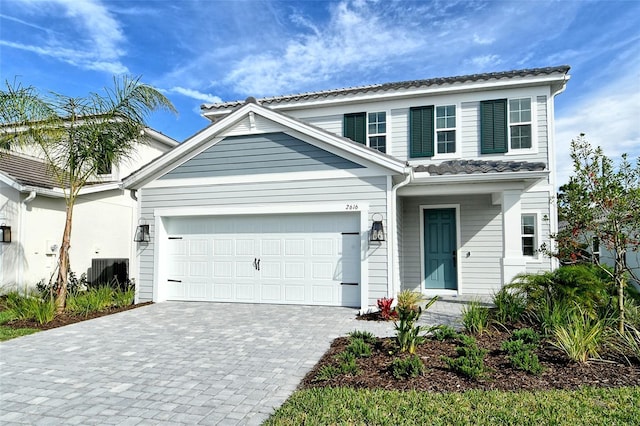 traditional-style home featuring decorative driveway, an attached garage, and central AC unit