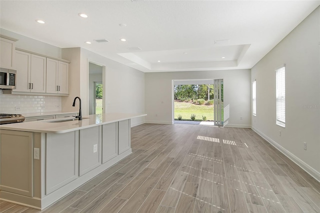 kitchen featuring stainless steel microwave, light countertops, decorative backsplash, a raised ceiling, and a sink