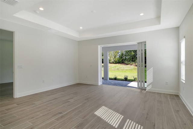 empty room featuring light wood finished floors, visible vents, and a tray ceiling