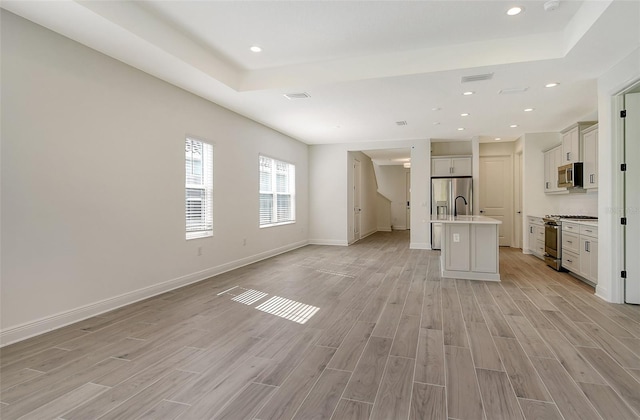 interior space with baseboards, open floor plan, light wood finished floors, and stainless steel appliances