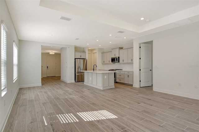 unfurnished living room with light wood finished floors, visible vents, baseboards, and a sink