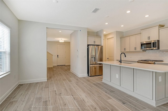 kitchen with visible vents, wood tiled floor, a sink, stainless steel appliances, and backsplash