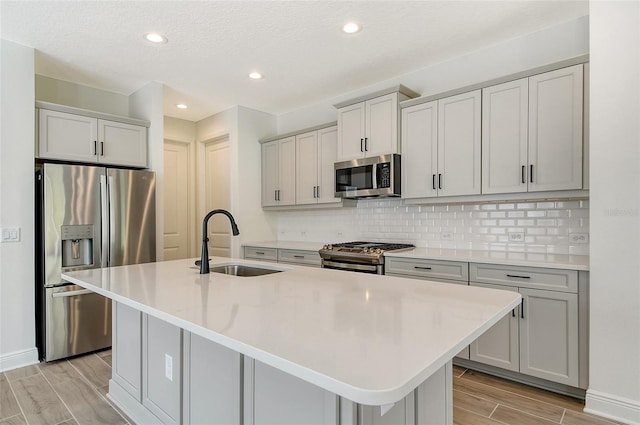 kitchen with backsplash, wood finish floors, a center island with sink, appliances with stainless steel finishes, and a sink