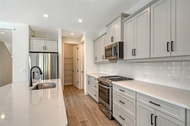 kitchen featuring wood tiled floor, light stone counters, decorative backsplash, appliances with stainless steel finishes, and a sink