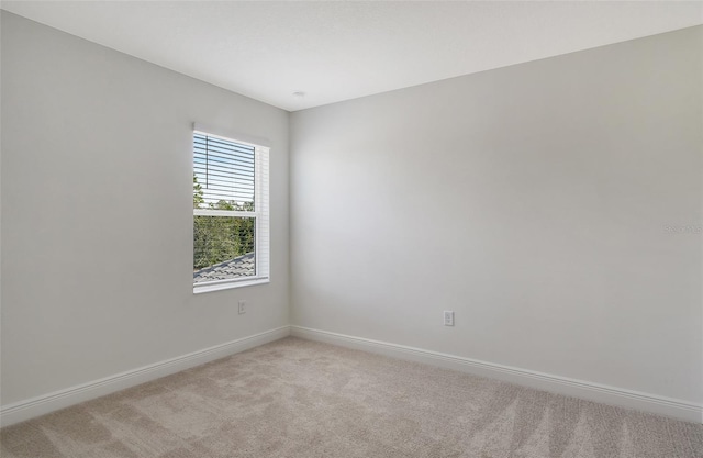 spare room featuring light carpet and baseboards