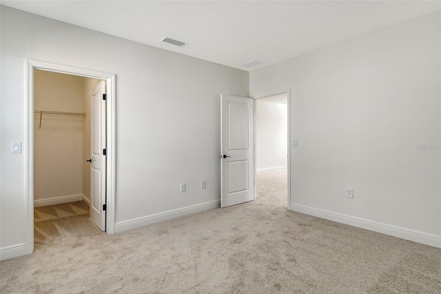 unfurnished bedroom with a spacious closet, visible vents, baseboards, and carpet