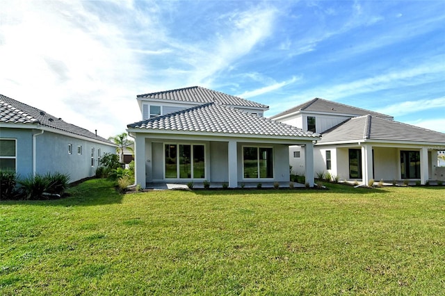 rear view of property with a lawn, a tiled roof, and stucco siding