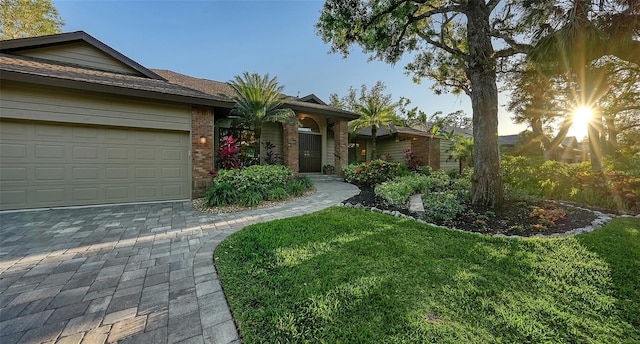 ranch-style home featuring a front lawn, decorative driveway, brick siding, and a garage