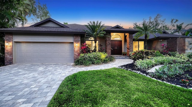 ranch-style home featuring decorative driveway, brick siding, an attached garage, and a lawn