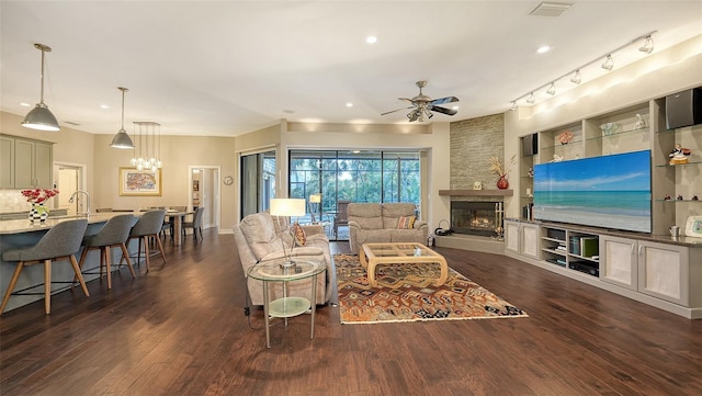 living area featuring ceiling fan with notable chandelier, dark wood-style floors, visible vents, and a fireplace