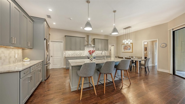 kitchen with dark wood-style floors, gray cabinets, a sink, wall chimney exhaust hood, and stainless steel fridge