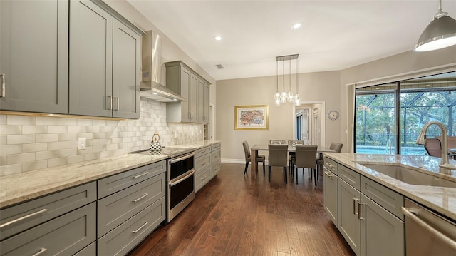 kitchen featuring gray cabinetry, a sink, stainless steel appliances, wall chimney range hood, and decorative backsplash