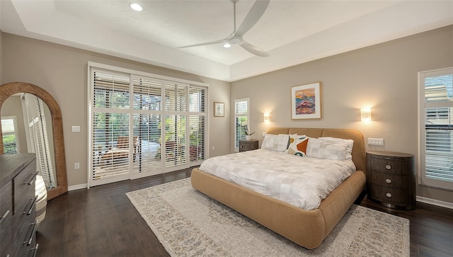 bedroom with dark wood-style flooring, multiple windows, a raised ceiling, and access to outside