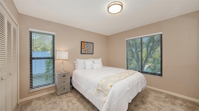 bedroom with a closet, baseboards, light colored carpet, and a textured ceiling