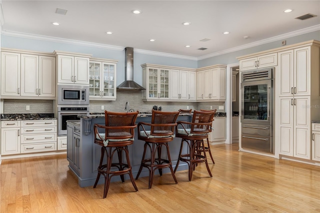 137 Big Pass Ln, Sarasota, FL 34242 - kitchen with a kitchen island, wall chimney exhaust hood, a kitchen breakfast bar, appliances with stainless steel finishes, and light wood-style flooring
