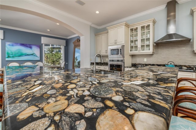 137 Big Pass Ln, Sarasota, FL 34242 - kitchen featuring a sink, cream cabinetry, wall chimney exhaust hood, stainless steel appliances, and arched walkways