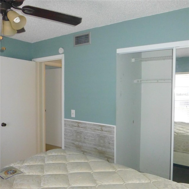 bedroom featuring a wainscoted wall, visible vents, ceiling fan, a closet, and a textured ceiling