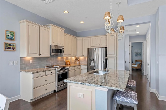 kitchen with a sink, appliances with stainless steel finishes, cream cabinets, a notable chandelier, and tasteful backsplash