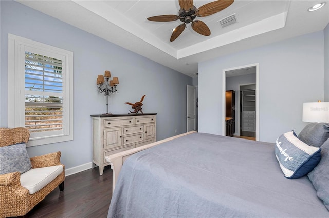 bedroom featuring visible vents, a ceiling fan, a tray ceiling, dark wood-style floors, and baseboards