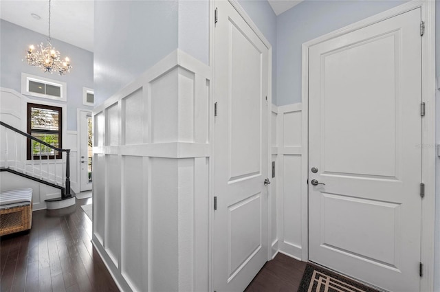 entrance foyer with a wainscoted wall, dark wood finished floors, stairs, a decorative wall, and a chandelier