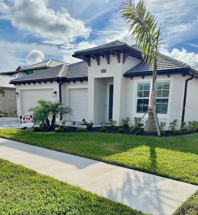 view of front of property featuring a tiled roof, concrete driveway, a front yard, stucco siding, and a garage