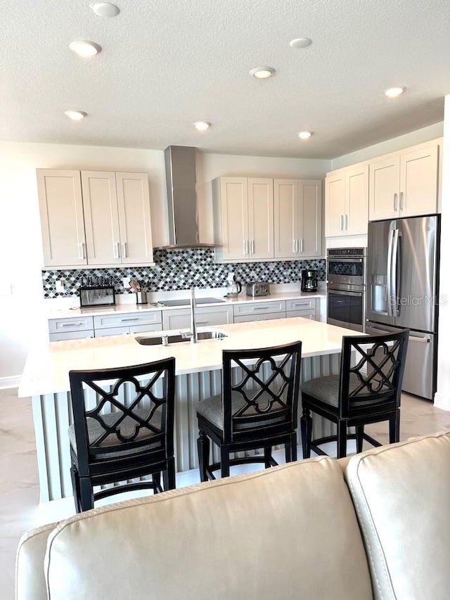 kitchen featuring a kitchen bar, stainless steel appliances, wall chimney exhaust hood, and light countertops