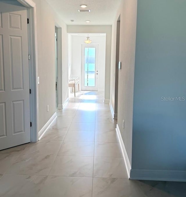 hallway with light tile patterned flooring, visible vents, and baseboards