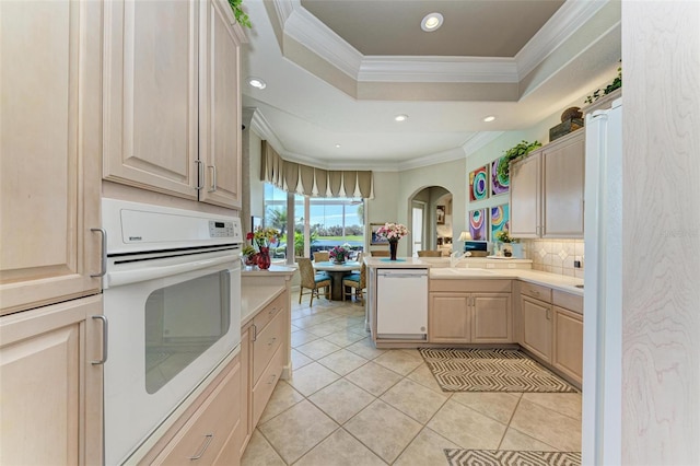 kitchen featuring light brown cabinets, light countertops, ornamental molding, white appliances, and a raised ceiling