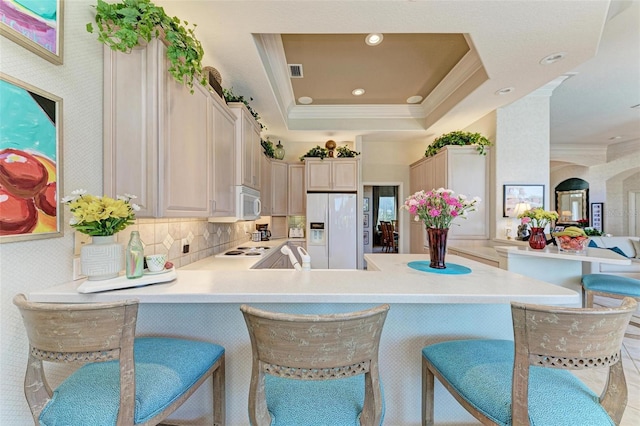 kitchen with crown molding, a kitchen breakfast bar, a peninsula, white appliances, and a raised ceiling