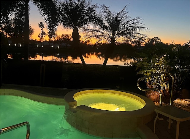 pool at dusk with an in ground hot tub and a water view