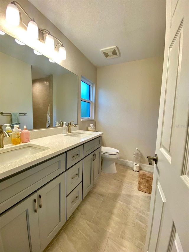 bathroom with double vanity, toilet, baseboards, and a sink