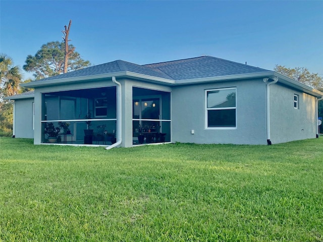 rear view of house featuring stucco siding, a yard, a sunroom, and roof with shingles