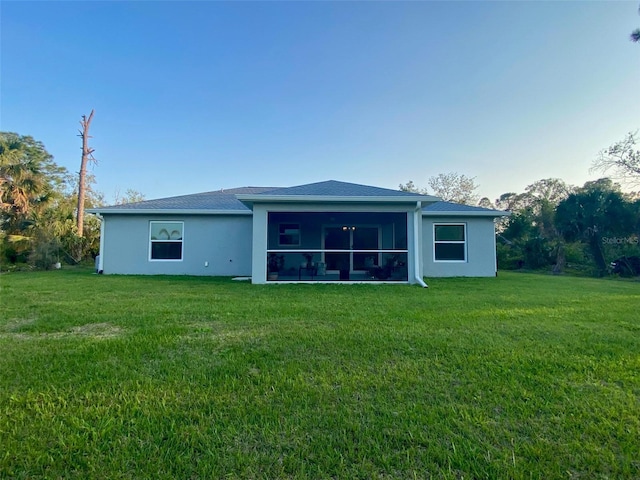 back of property with stucco siding, a lawn, and a sunroom