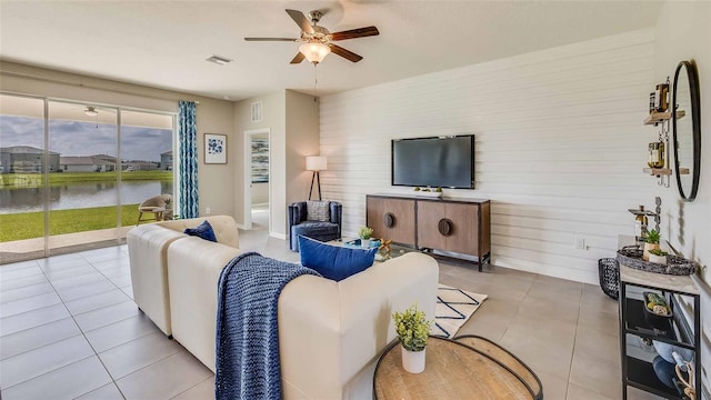 living room featuring ceiling fan, tile patterned floors, a water view, and wood walls
