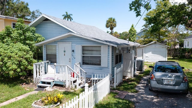 view of front of home featuring roof with shingles, a detached garage, an outdoor structure, and fence